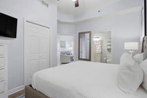 A bedroom with a large bed, a television, a wardrobe, a mirror, and a bathroom visible through an open door. - Phoenix 6 102 (Orange Beach)