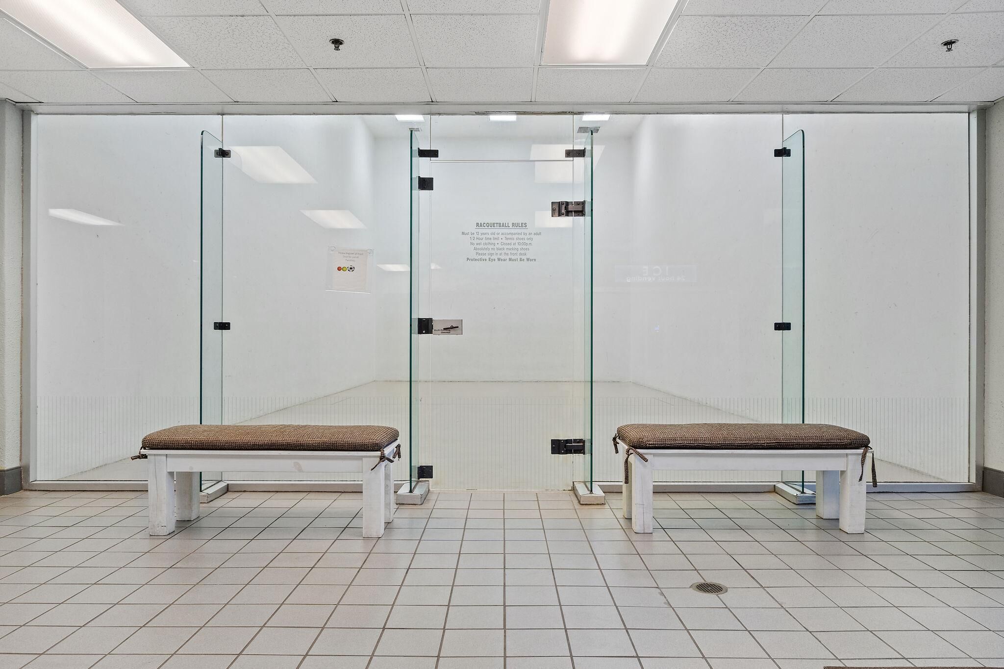 Ein Raum mit zwei weißen Bänken, einer Glastrennwand und einem an der Wand befestigten Schild mit Regeln.