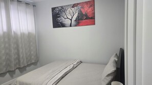 Une chambre à coucher avec un lit, un tableau, une fenêtre avec des rideaux et une table de chevet.