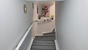 A staircase with a white handrail, grey steps, and a wall with a painting and two wall-mounted decorations. - Serene Modern Suite | 2BR, Trail & Nearby Lake (Spruce Grove)
