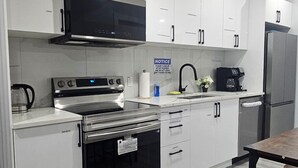 A modern kitchen with white cabinetry, stainless steel appliances, a built-in oven, and a coffee maker. - Serene Modern Suite | 2BR, Trail & Nearby Lake (Spruce Grove)