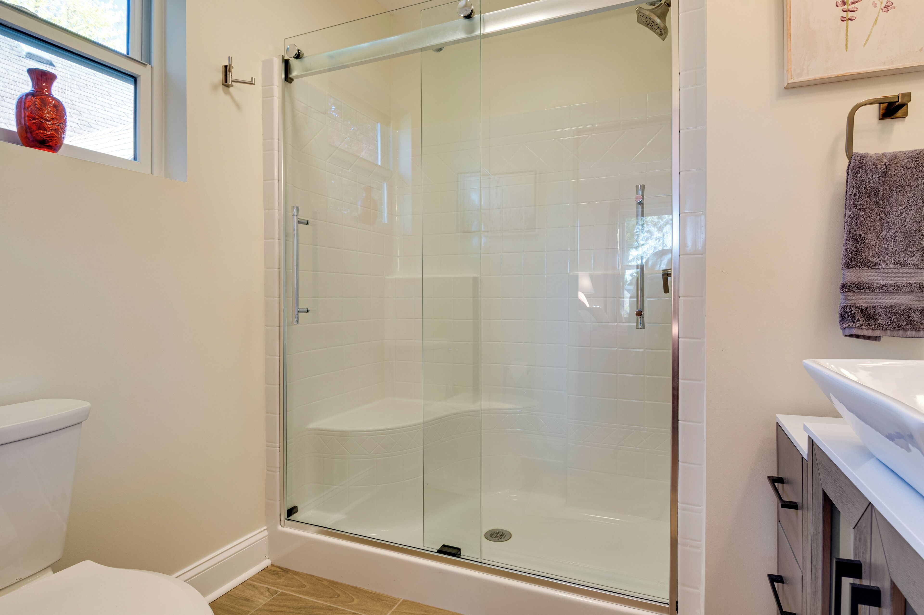 A modern bathroom with a glass-enclosed shower, white tiles, a toilet, and a sink with a towel rack.