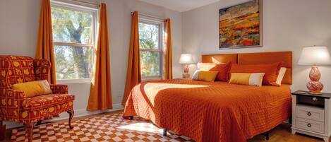 A bedroom with a checkered floor, a bed with orange bedding, a chair with a yellow cushion, and a painting on the wall.