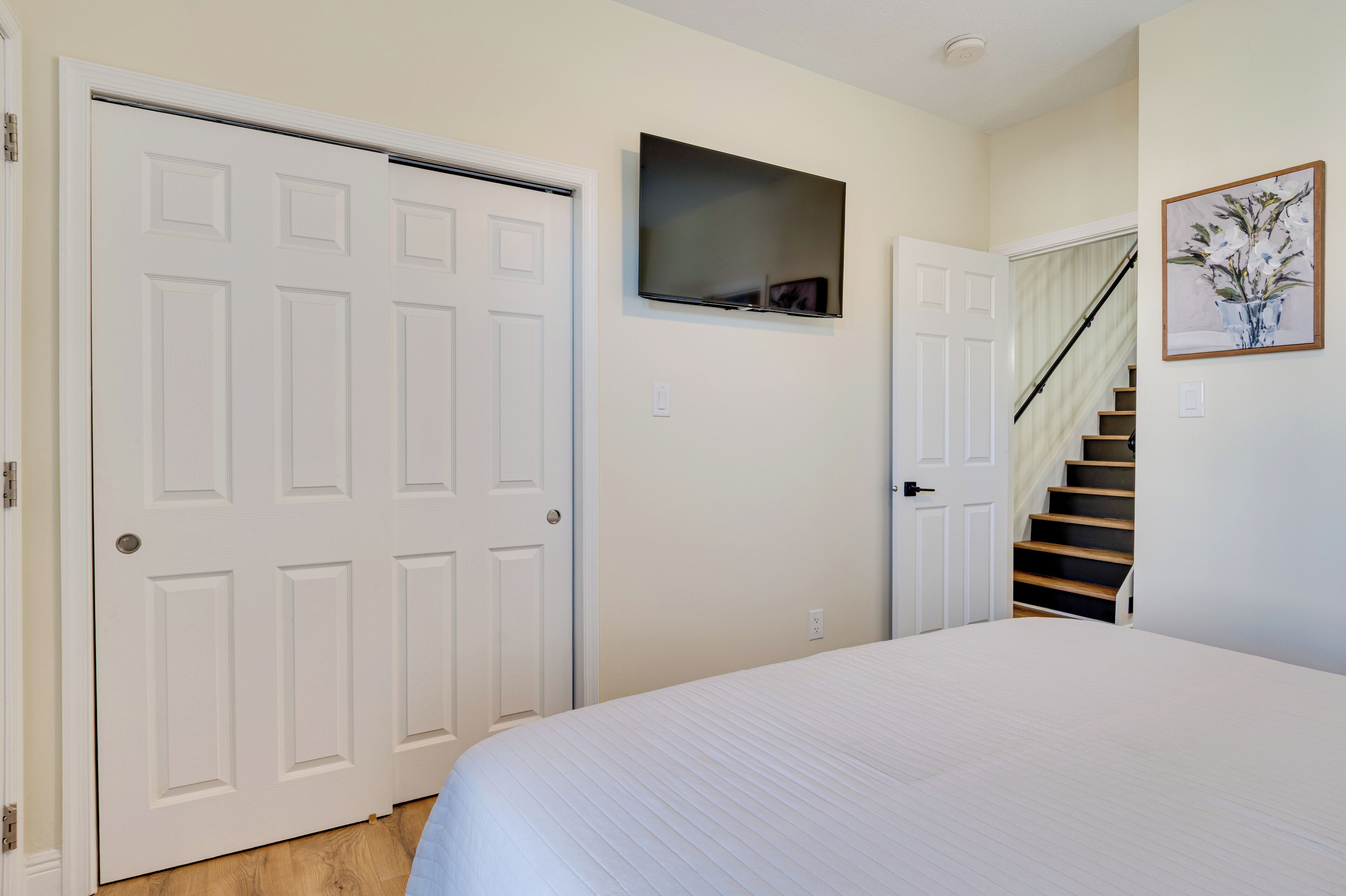 A bedroom with a bed, a TV mounted on the wall, a staircase, and a door.