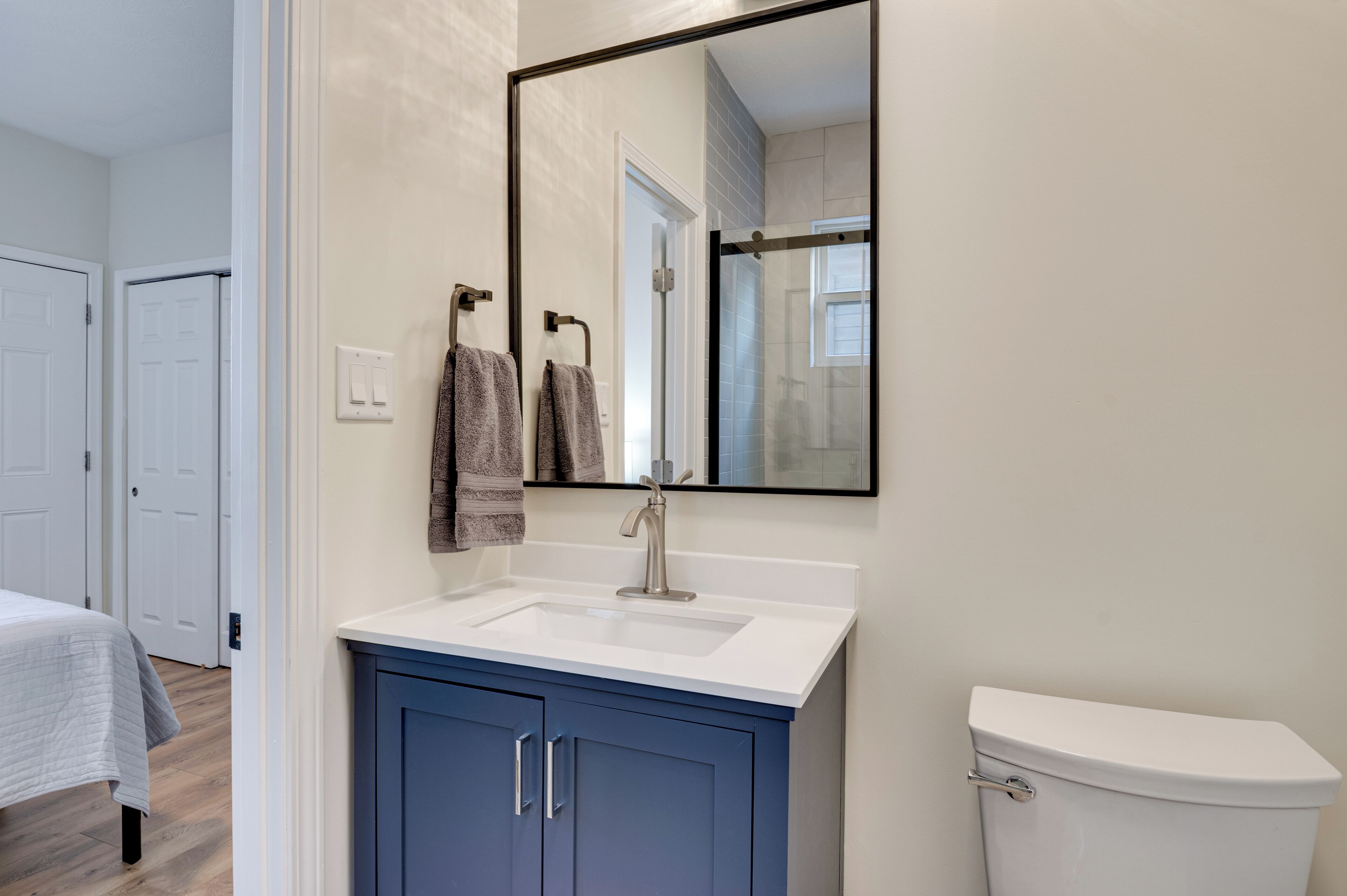 A bathroom with a white sink, blue cabinets, a toilet, and a mirror reflecting a shower area.