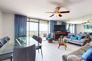 Una sala de estar moderna con una mesa de comedor de vidrio, asientos cómodos, un sofá y un ventilador de techo.