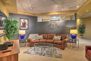 A modern living room with a brown leather sofa, a glass coffee table, and a large mirror on the wall. There are two lamps on side tables, a potted plant, and a framed picture on the wall. - Dtwn Anchorage Getaway: 2 Adjoining Condos! (Anchorage)