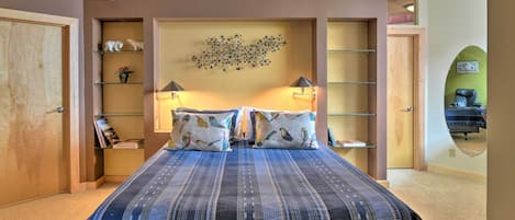 Un dormitorio con una cama grande, dos lámparas de noche, una lámpara de techo y una repisa con objetos decorativos.