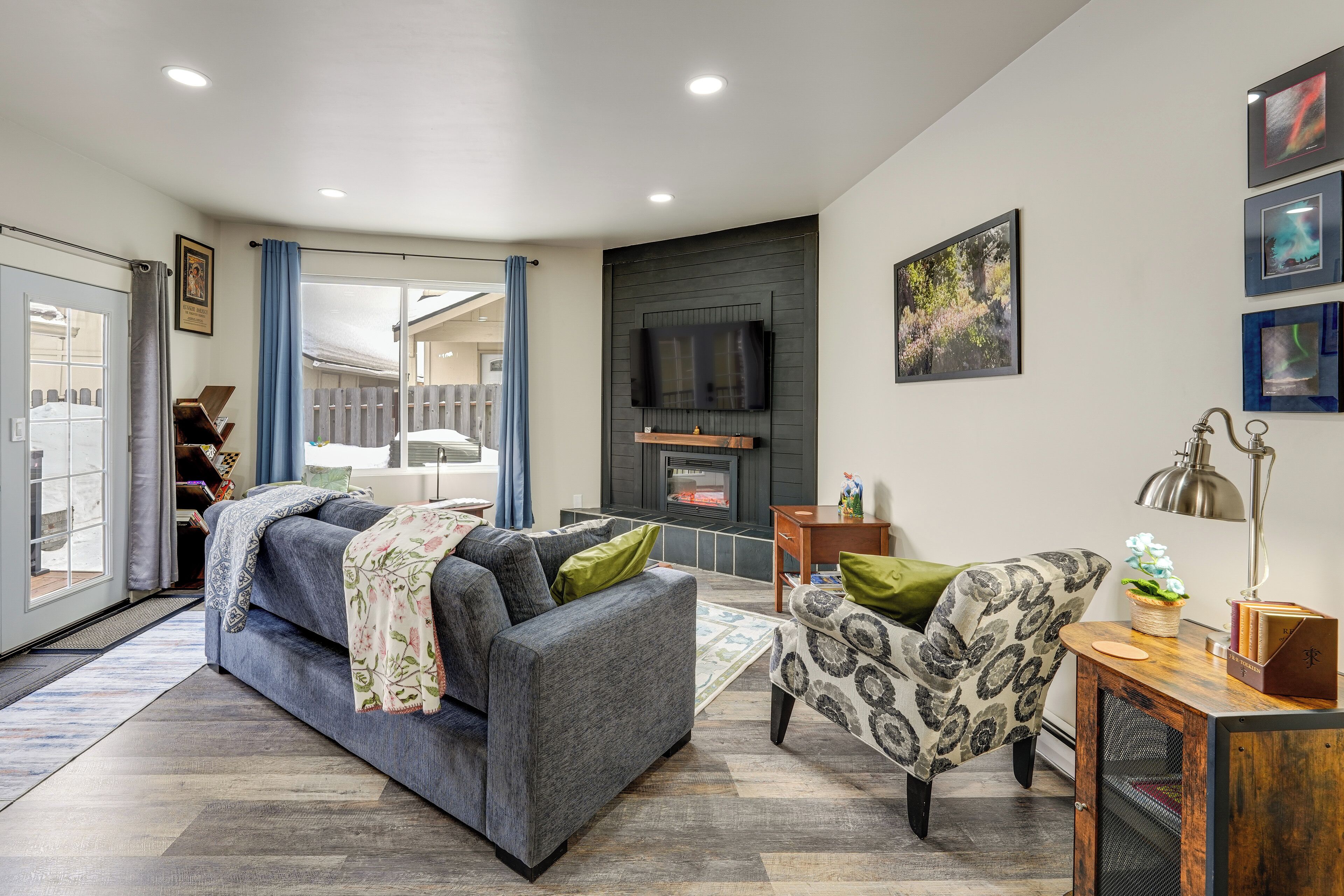 A modern living room with a sofa, armchair, fireplace, television, and artwork.