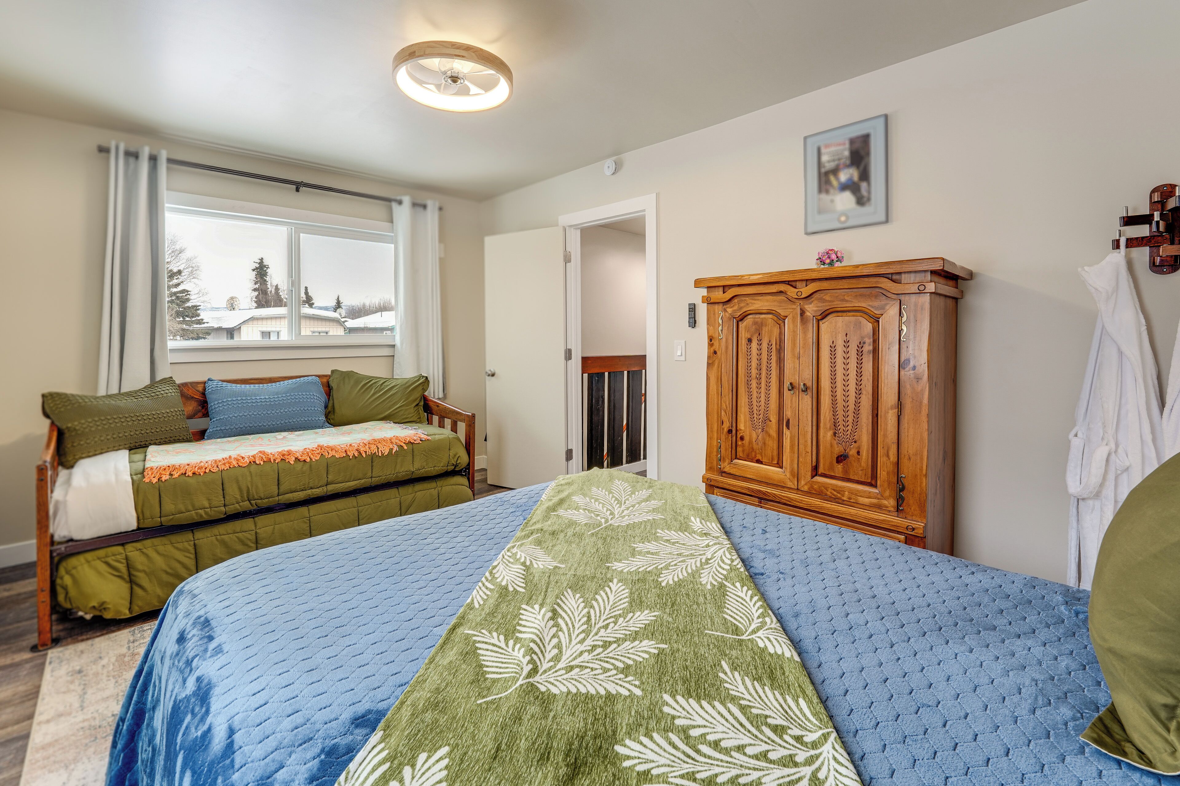 Une chambre à coucher avec un lit, une armoire en bois, une fenêtre et une porte.