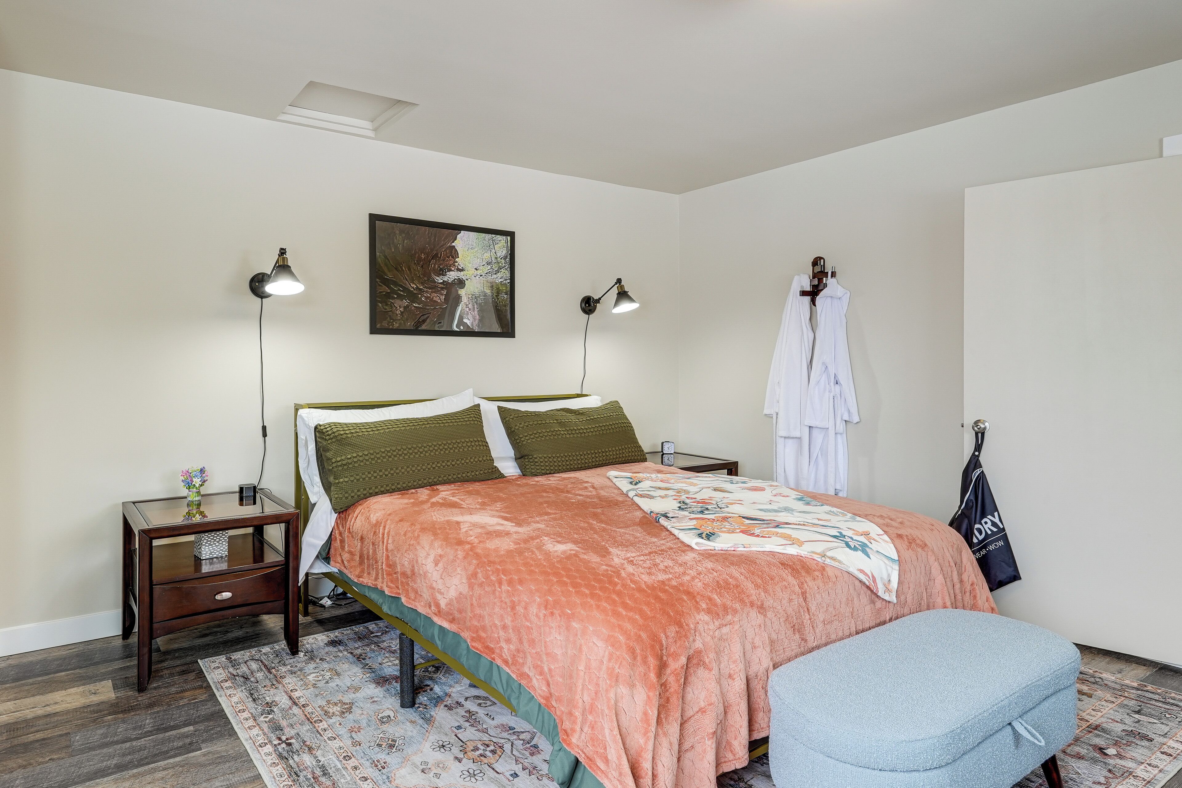 A bedroom with a bed, bedside lamps, a nightstand, a hanging robe, and a patterned rug.