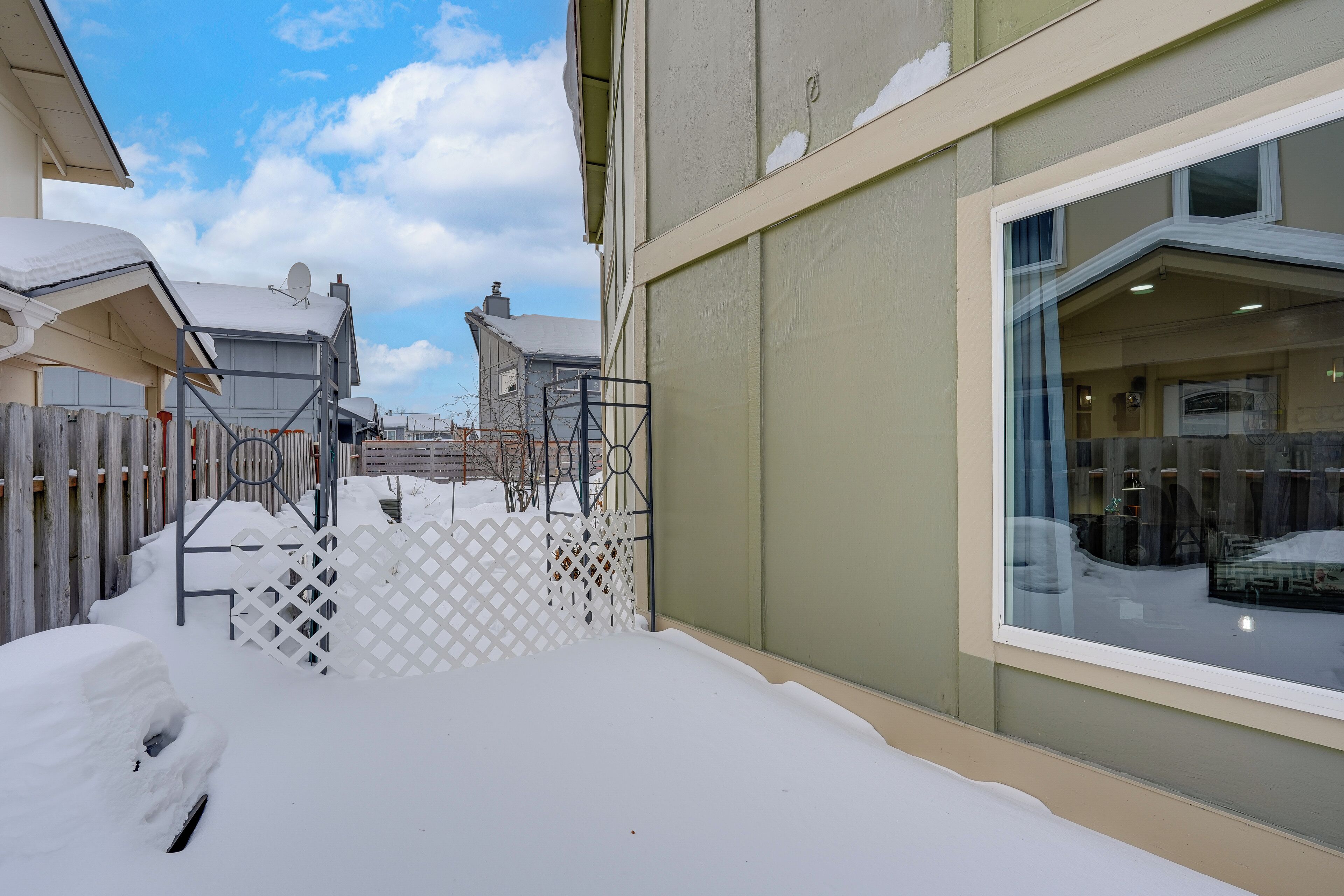 A snow-covered outdoor area with a white fence, a window with a view of the interior, and a building with a light-colored exterior.