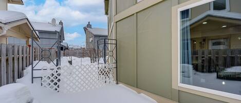 A snow-covered outdoor area with a white fence, a window with a view of the interior, and a building with a light-colored exterior.
