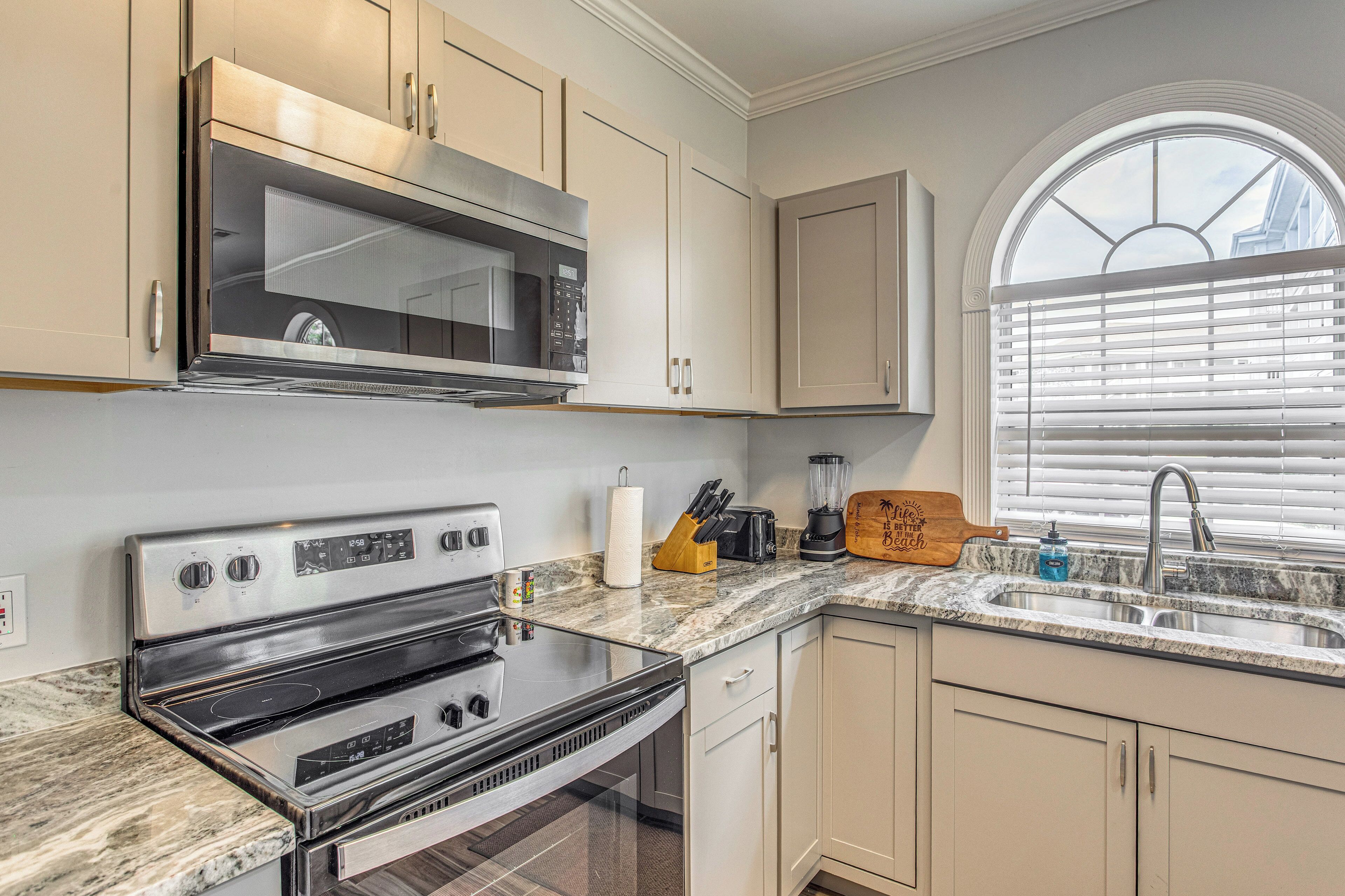 A kitchen with a microwave, stove, sink, and a window with blinds.