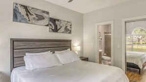 A bedroom with a large bed, a wooden headboard, two wall-mounted artworks, a bedside lamp, and a view through an open door. - Family Favorite 1st Floor Pool Golf (Myrtle Beach)