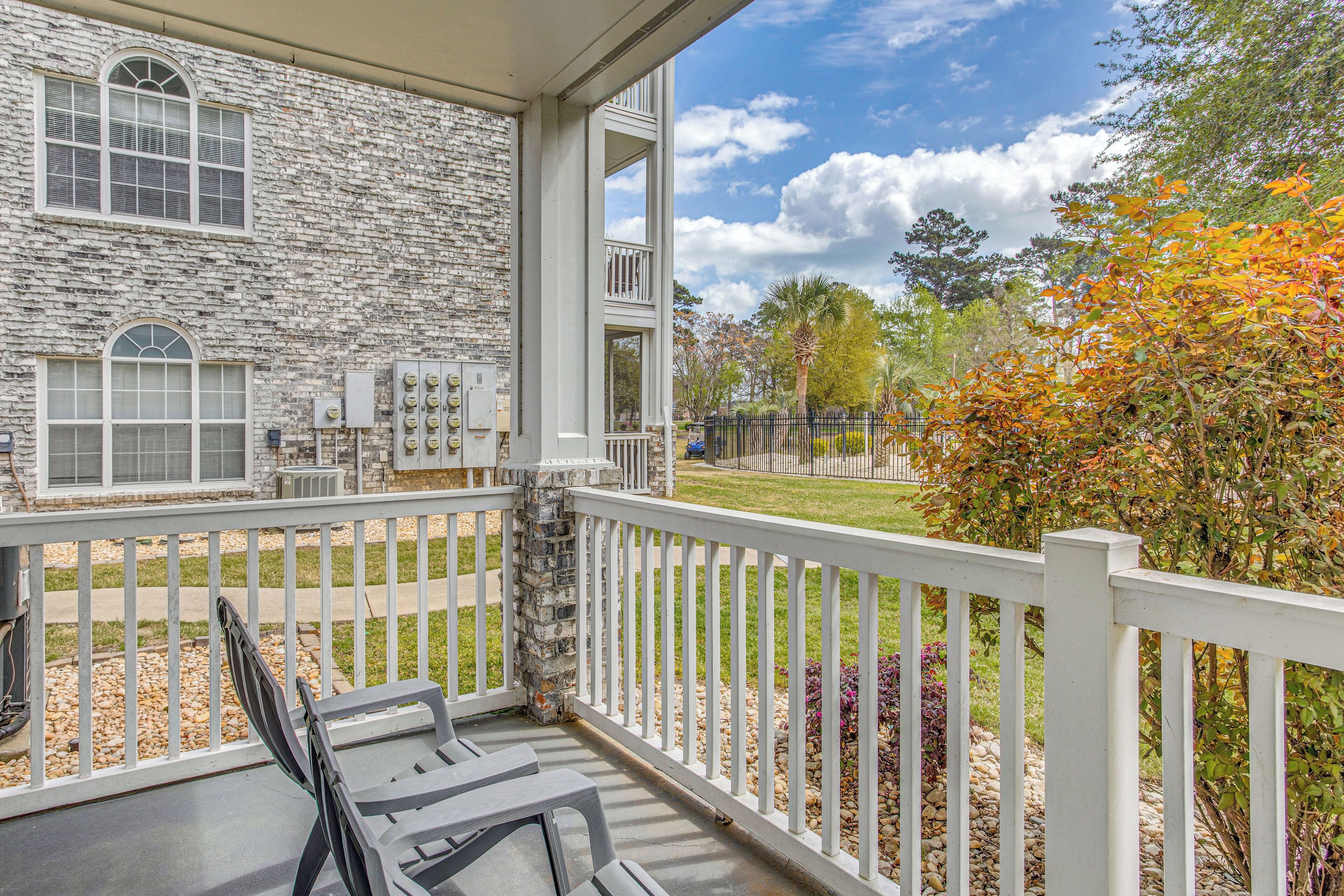A stone building with a balcony, outdoor seating, and a fenced yard with trees and shrubs.