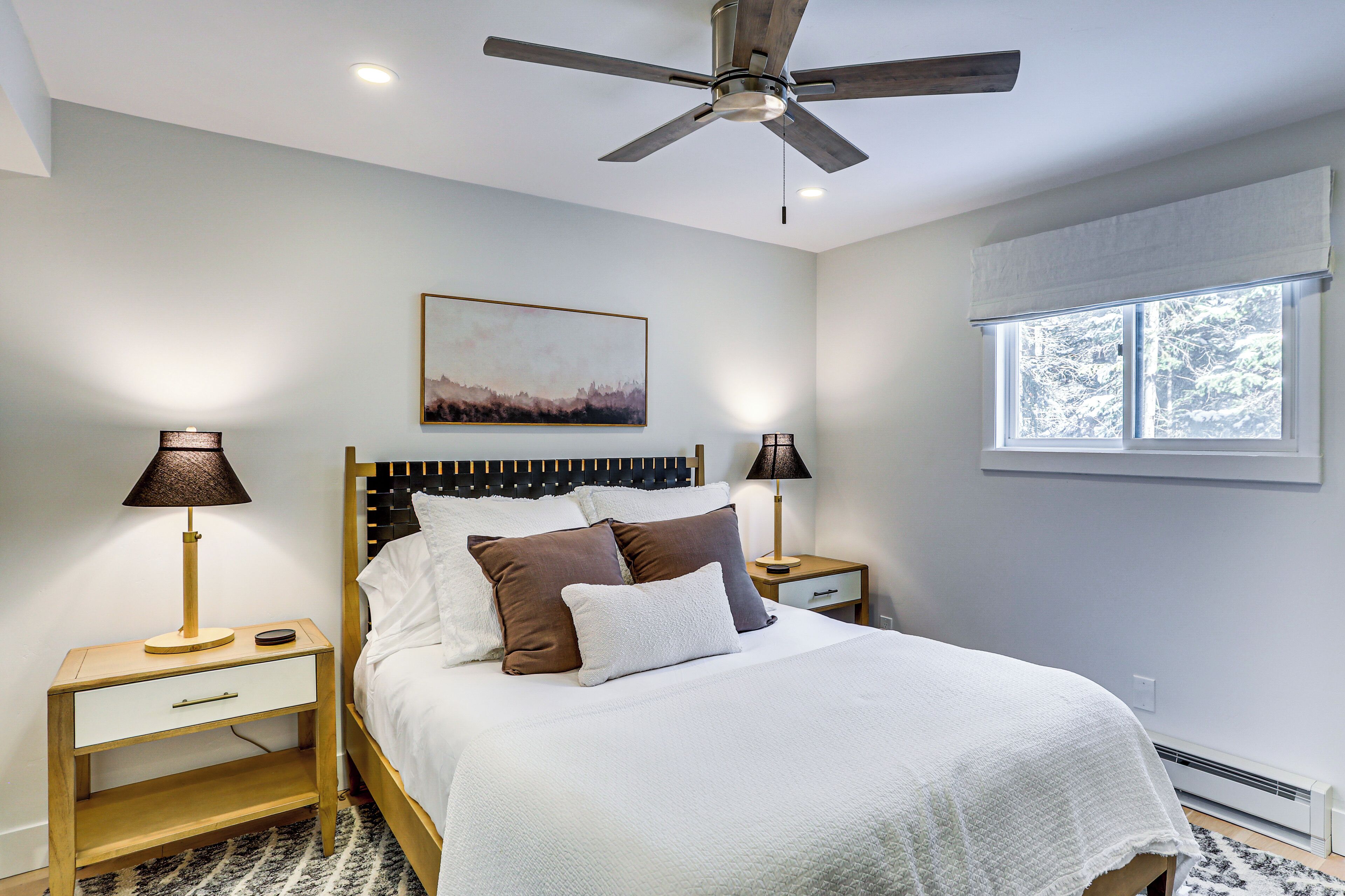 A bedroom with a bed, two bedside tables, a ceiling fan, a window, and a painting on the wall.