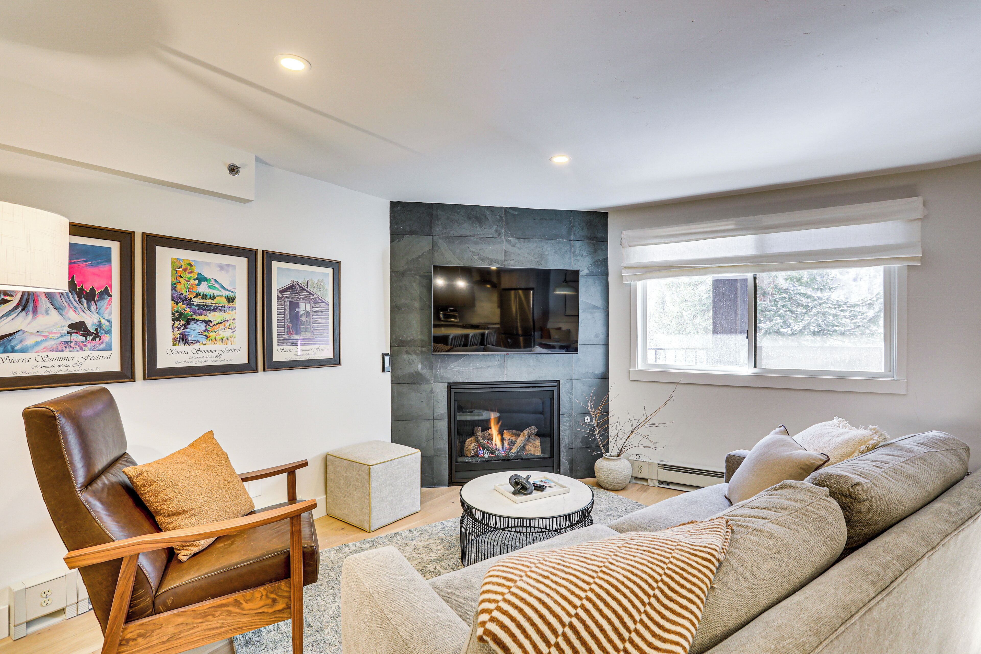 A modern living room with a fireplace, a leather armchair, a sofa, and framed artwork on the wall.