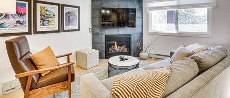 A modern living room with a fireplace, a leather armchair, a sofa, and framed artwork on the wall.