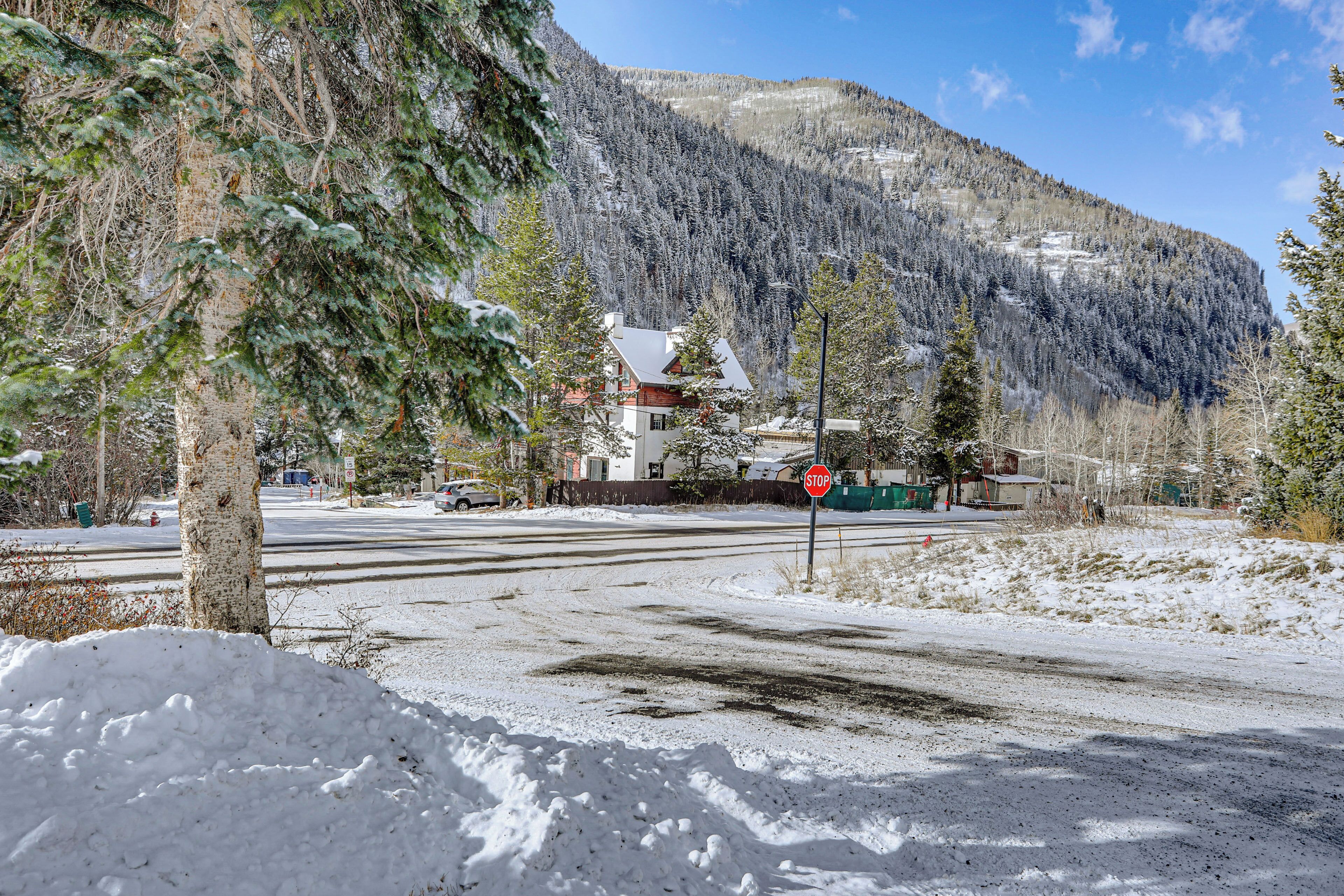 Paisaje nevado con una señal de parada, árboles y un edificio al fondo.