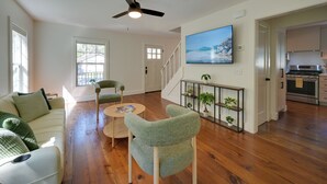 A living room with a sofa, chairs, a coffee table, a TV, a ceiling fan, and a staircase leading to a kitchen. - 5 Mi to Pier Village: Coastal Jade Cottage (St. Simons Island)