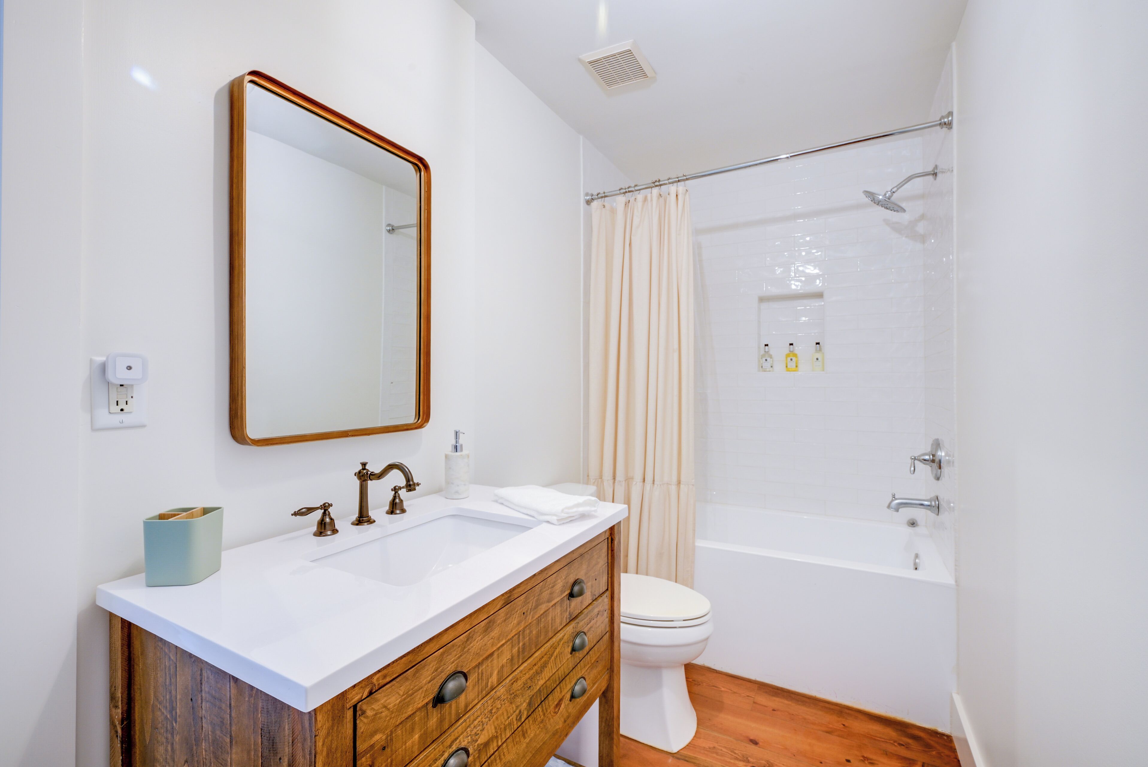 A bathroom with a wooden vanity, a white sink, a mirror, a toilet, and a shower area.