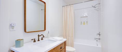 A bathroom with a wooden vanity, a white sink, a mirror, a toilet, and a shower area.