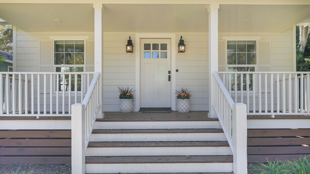 A white building with a front porch, steps leading to a door, and two potted plants on either side. - 5 Mi to Pier Village: Coastal Jade Cottage (St. Simons Island)