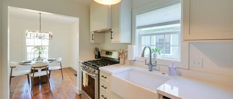 A modern kitchen with white cabinetry, a stainless steel stove, and a large window.