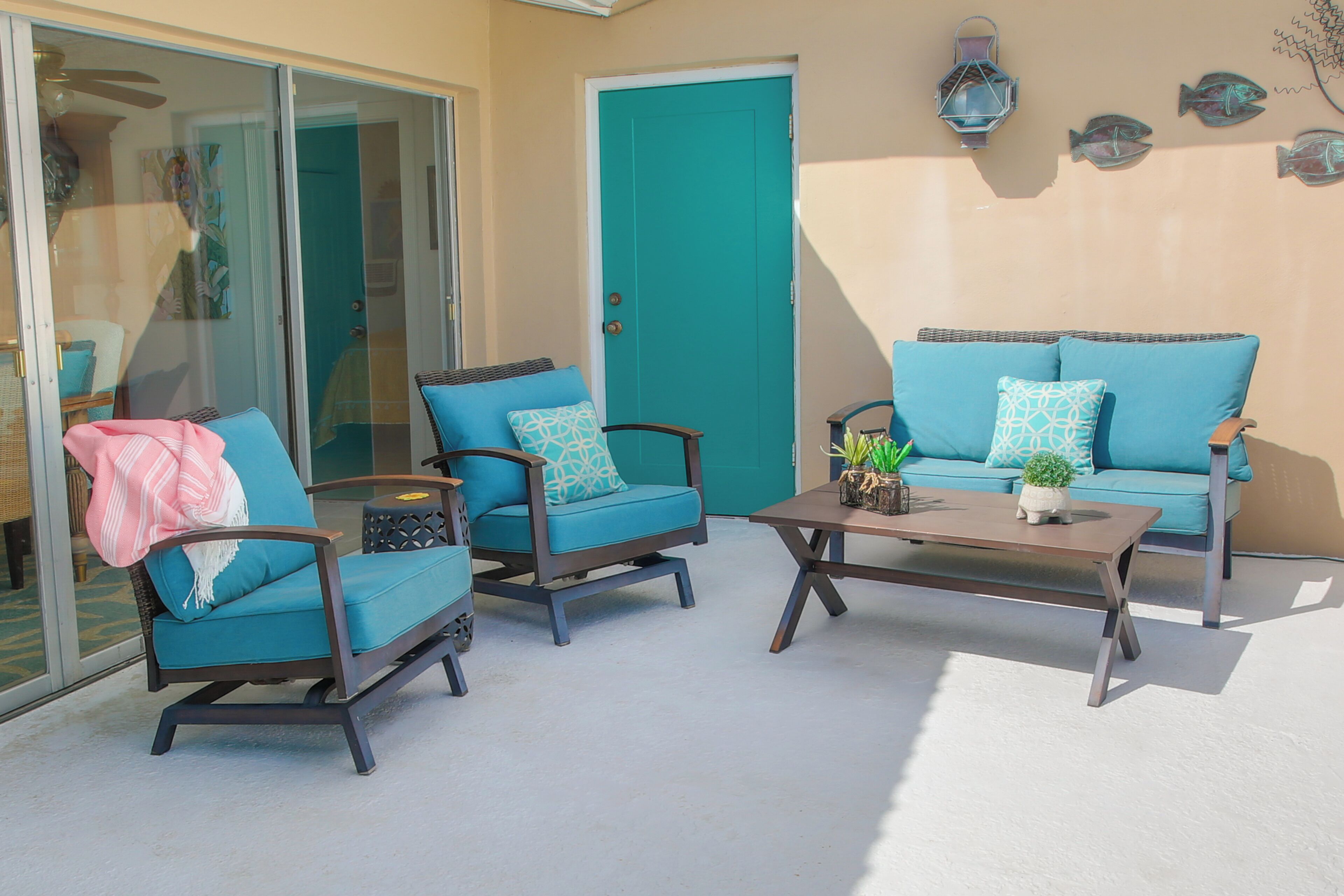 A patio with two blue chairs, a brown table, and a teal door.