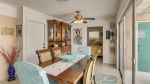 Un espace repas comprenant une table en bois, des chaises, un ventilateur de plafond et une porte vitrée.