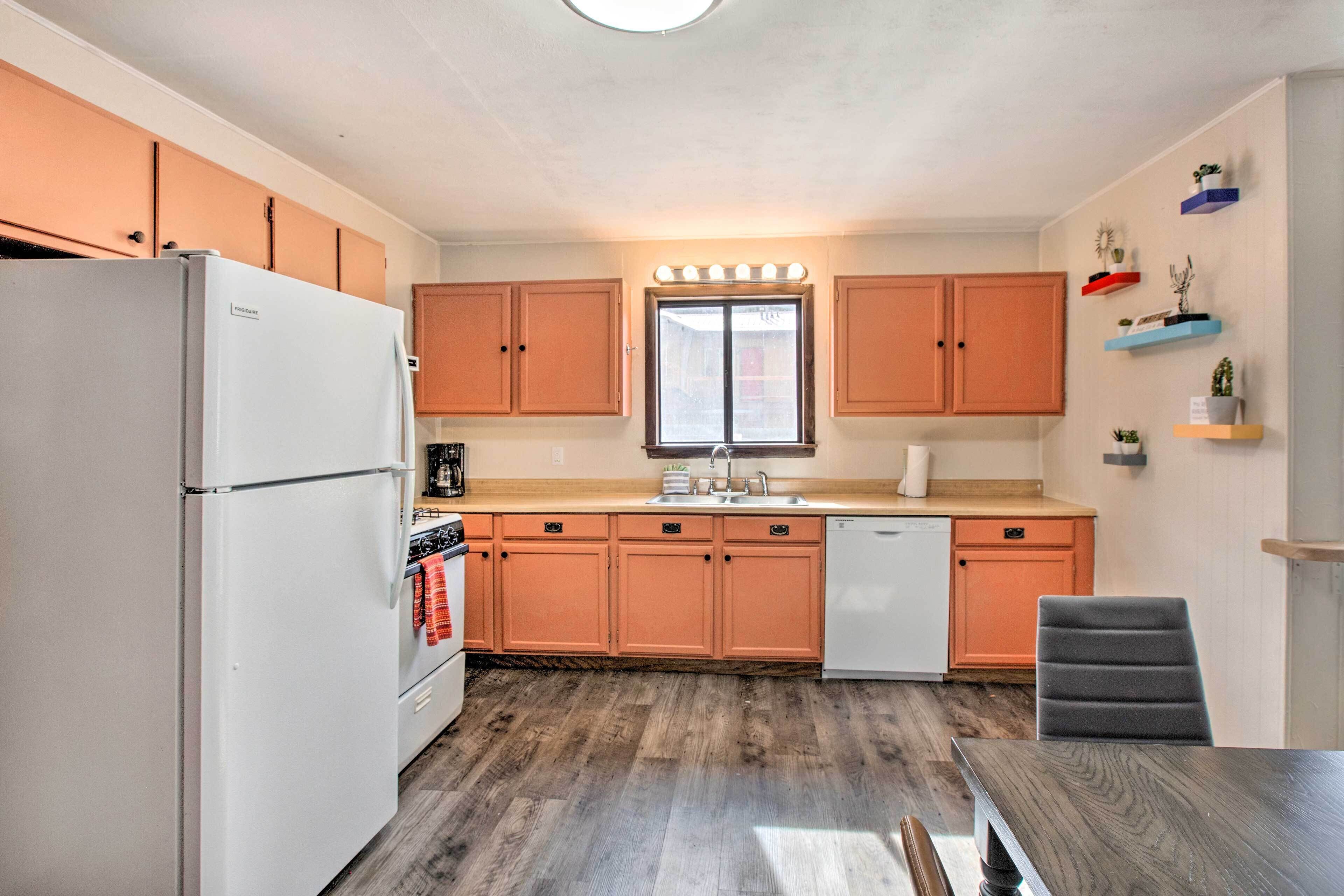A kitchen with wooden cabinets, a refrigerator, a dishwasher, and a window with lights above the sink.