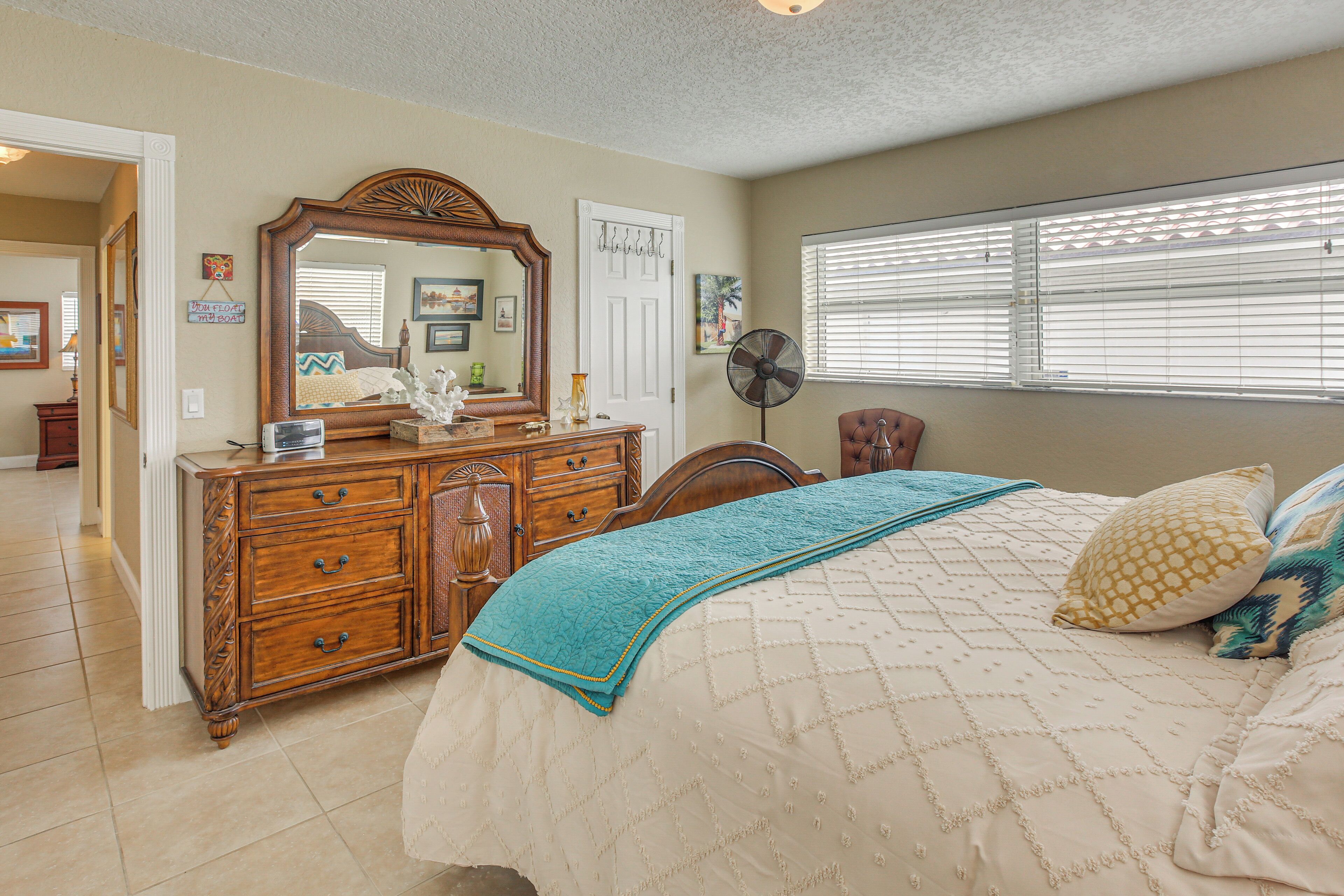 A bedroom with a bed, dresser, mirror, and window with blinds.