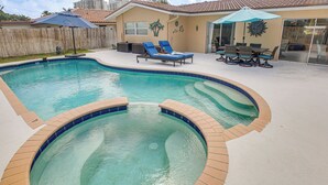Une piscine avec un jacuzzi, des chaises longues et un espace patio comprenant une table et des chaises.