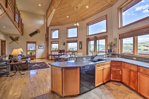A spacious kitchen with a large island, wooden cabinets, and a dishwasher. There are multiple windows providing views of the surrounding landscape. - 2 Mi to Granby Ranch: Granby Home w/ Hot Tub! (Granby)