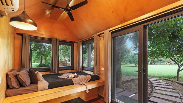 Ein Zimmer mit einem Bett, einem Deckenventilator, großen Fenstern und Blick ins Freie.