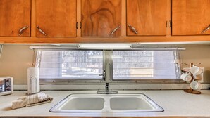 A kitchen with wooden cabinets, a double sink, a window with blinds, and a microwave. - 2 Mi to Midtown! All-season Base w/ Hot Tub Access (Ruidoso)