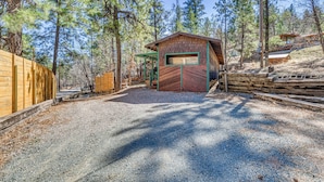 A rustic cabin with a gravel driveway, surrounded by tall pine trees. - 2 Mi to Midtown! All-season Base w/ Hot Tub Access (Ruidoso)