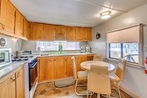 A kitchen with wooden cabinets, a stove, a microwave, a sink, and a dining area with a table and chairs. - 2 Mi to Midtown! All-season Base w/ Hot Tub Access (Ruidoso)