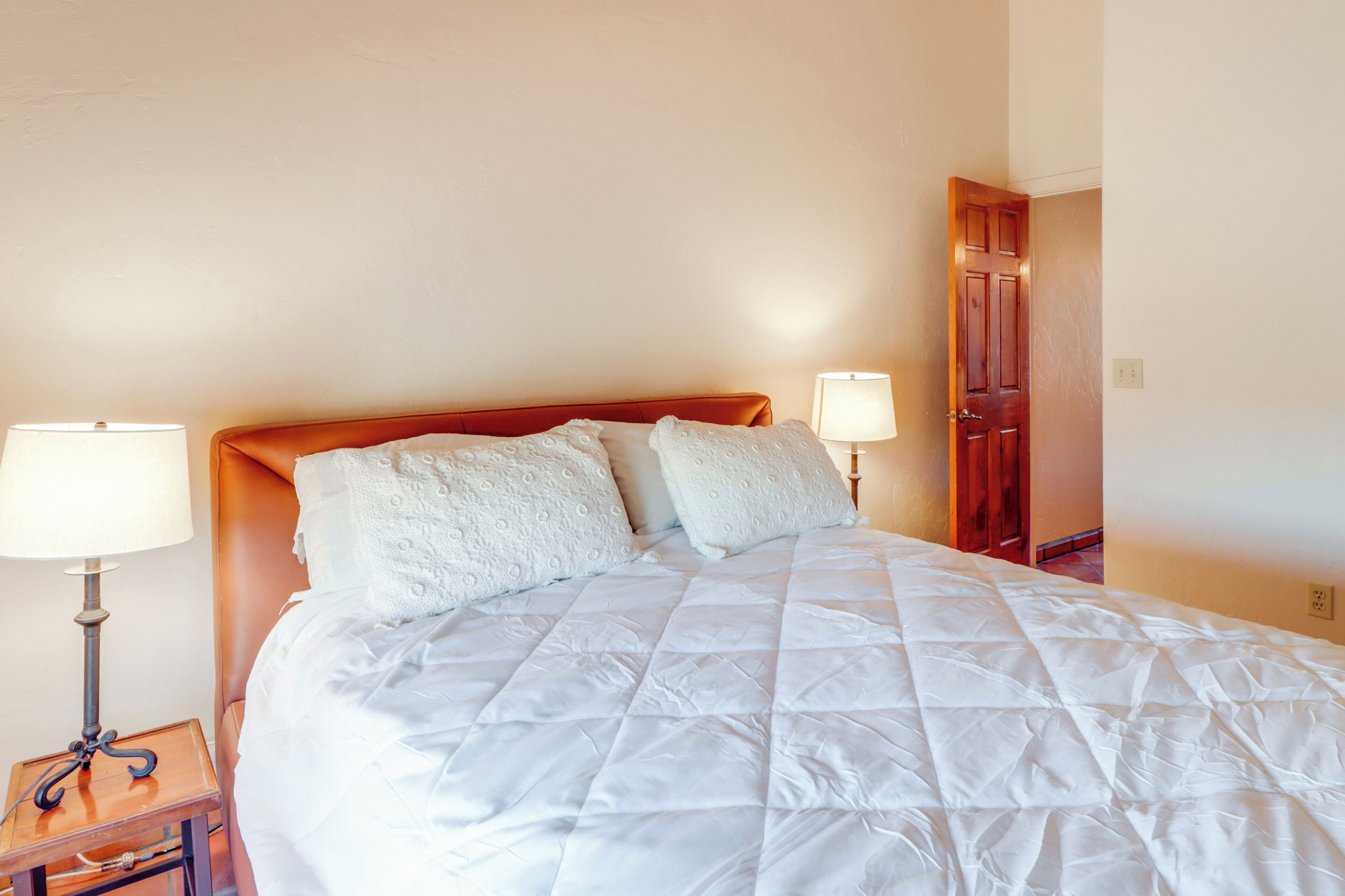 A neatly made bed with a white quilt, two bedside lamps, and a wooden headboard.