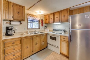 A kitchen with wooden cabinets, a stainless steel refrigerator, a stove, and a coffee maker. - Near Grindstone Lake & Family Fun! Cozy Cabin (Ruidoso)