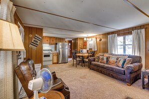 A cozy living room with a leather chair, a fan, a brown sofa with patterned cushions, a dining table with chairs, and a kitchen in the background. - Near Grindstone Lake & Family Fun! Cozy Cabin (Ruidoso)