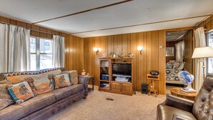 Ein gemütliches Wohnzimmer mit Ledersofa, Holzwandverkleidung, Fernseher und einem kleinen Ventilator.
