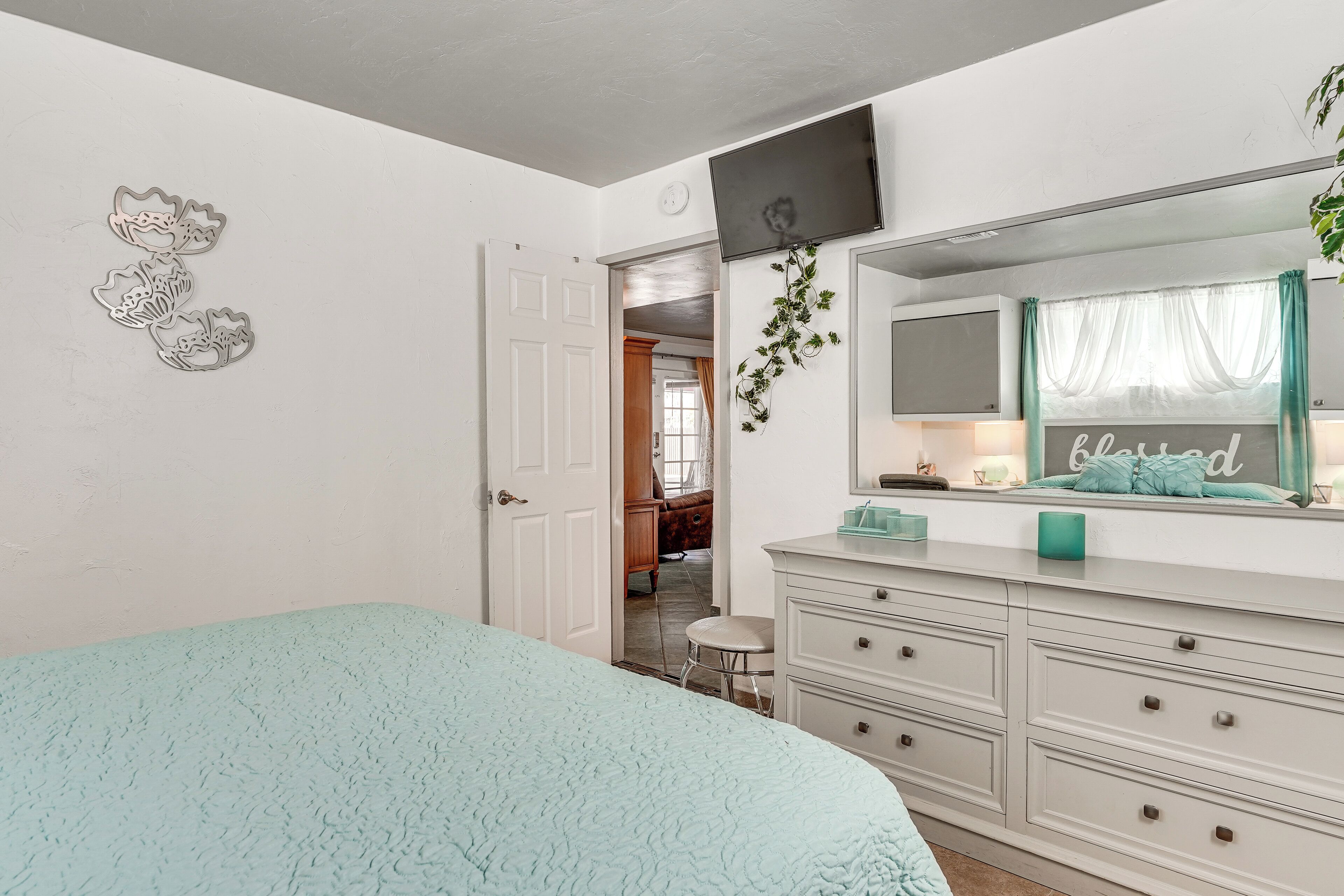 Un dormitorio con cama, cómoda, espejo y una puerta que da a otra habitación.