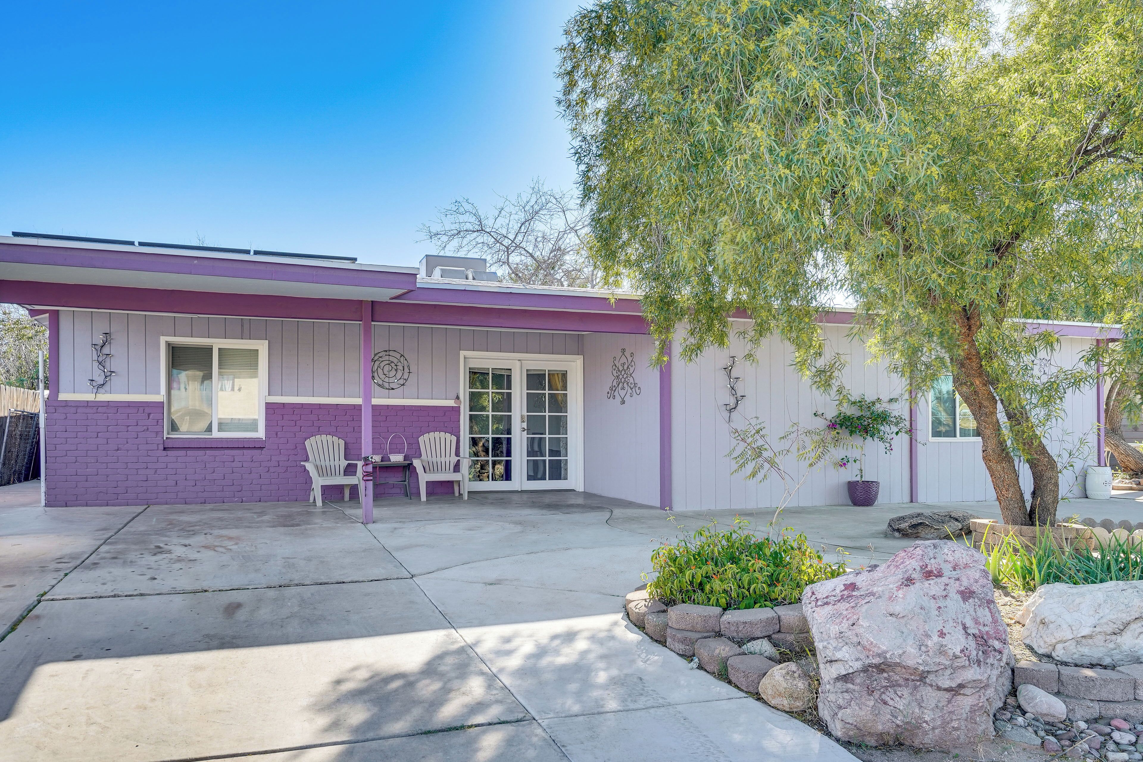 A house with a purple exterior, a covered patio, and a tree in the foreground.