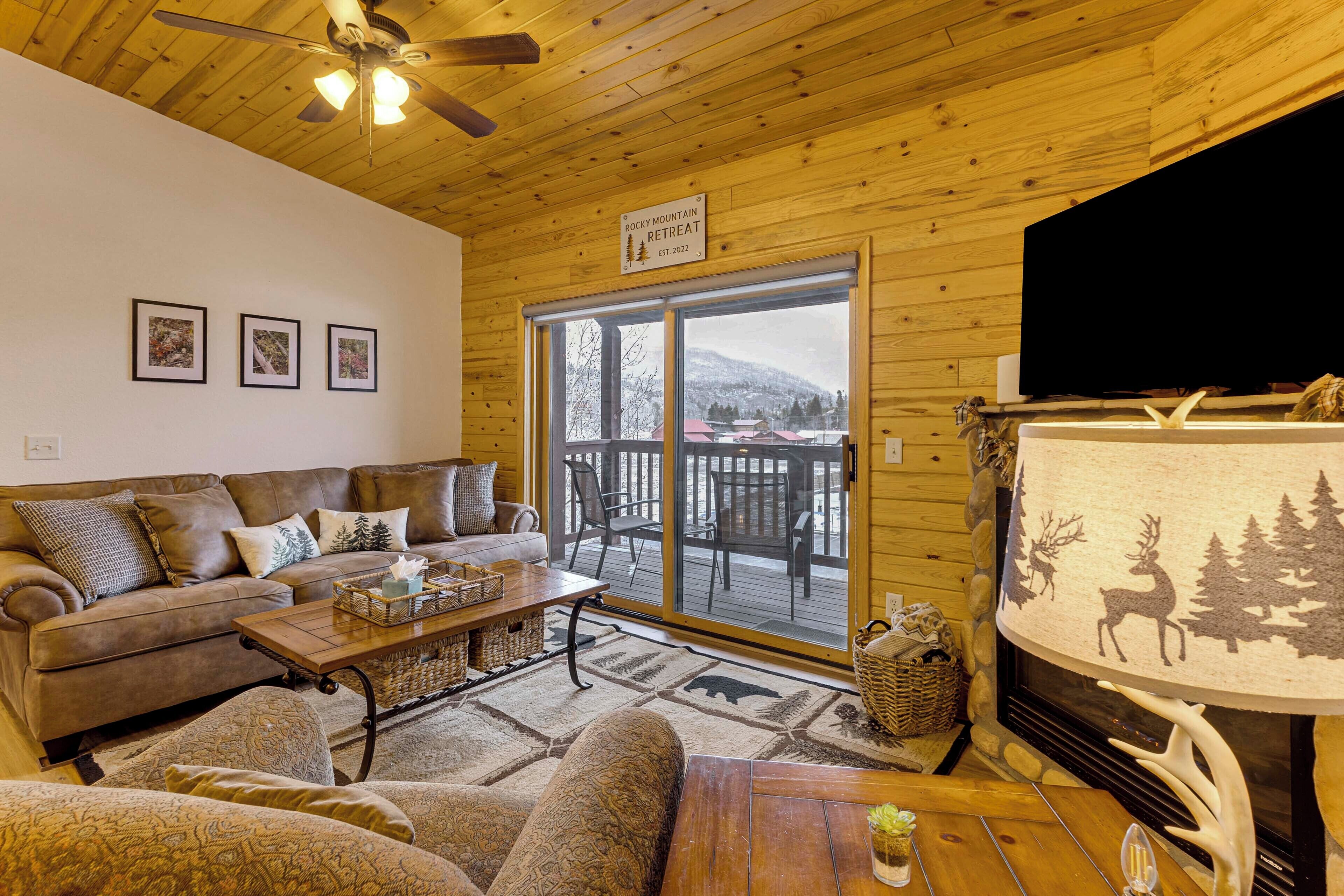 A cozy living room with a wooden ceiling, a sofa, a coffee table, and a fireplace with a deer and tree silhouette.