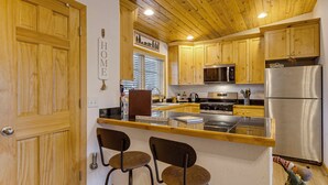 A kitchen with wooden cabinets, a stainless steel refrigerator, and two bar stools. - Rocky Mtn-view Retreat! Walk to Dtwn Grand Lake (Grand Lake)
