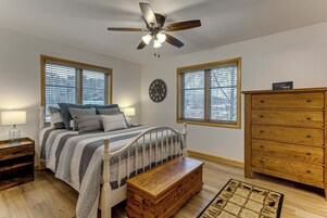A bedroom with a bed, a wooden dresser, a nightstand, a ceiling fan, and a wall clock.