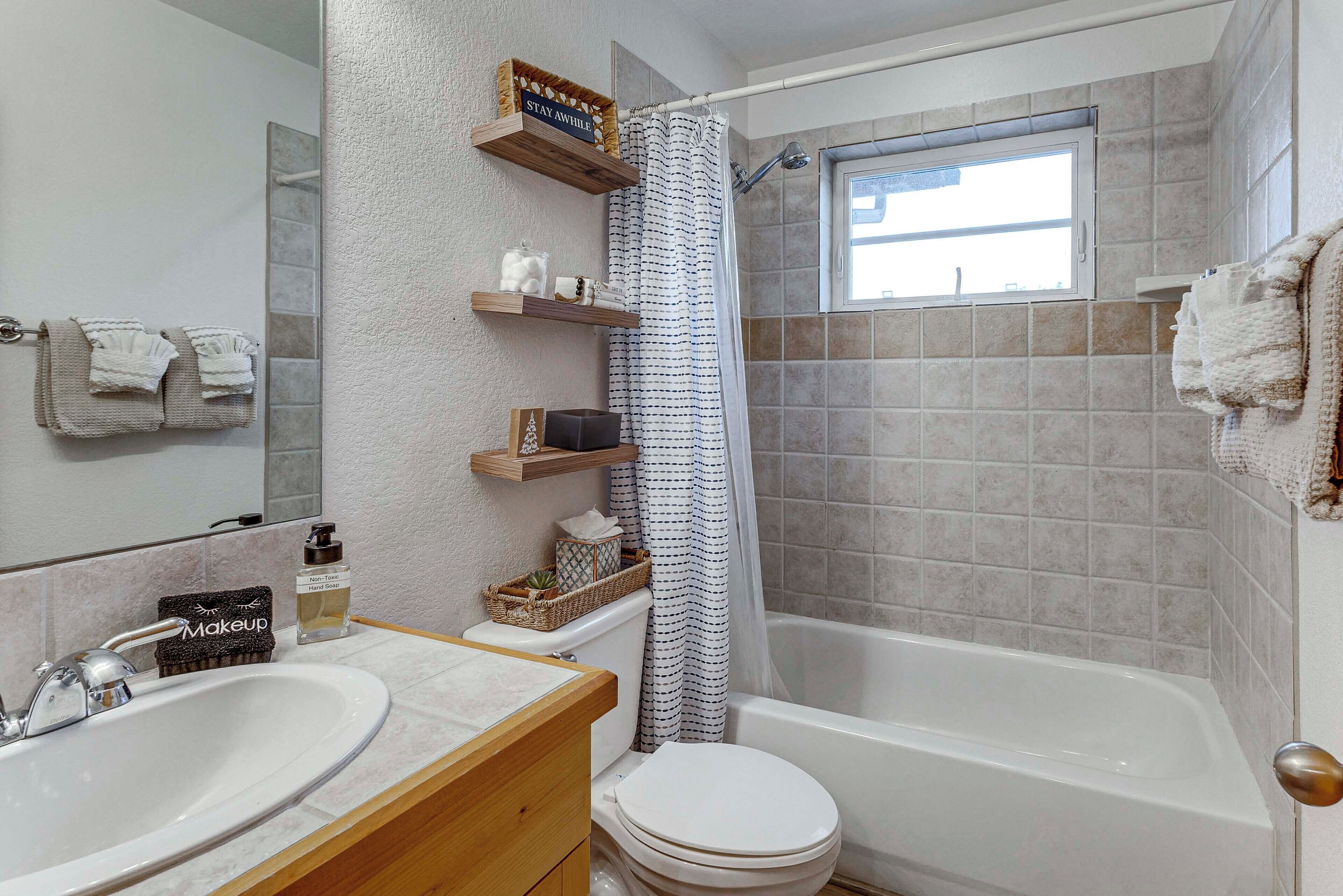 Un bagno con lavandino, WC e vasca da bagno. Sono presenti scaffali con articoli da toilette e una tenda da doccia.