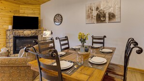 A dining area with a wooden table set for four, surrounded by chairs, a fireplace, and a wall-mounted clock. - Rocky Mtn-view Retreat! Walk to Dtwn Grand Lake (Grand Lake)
